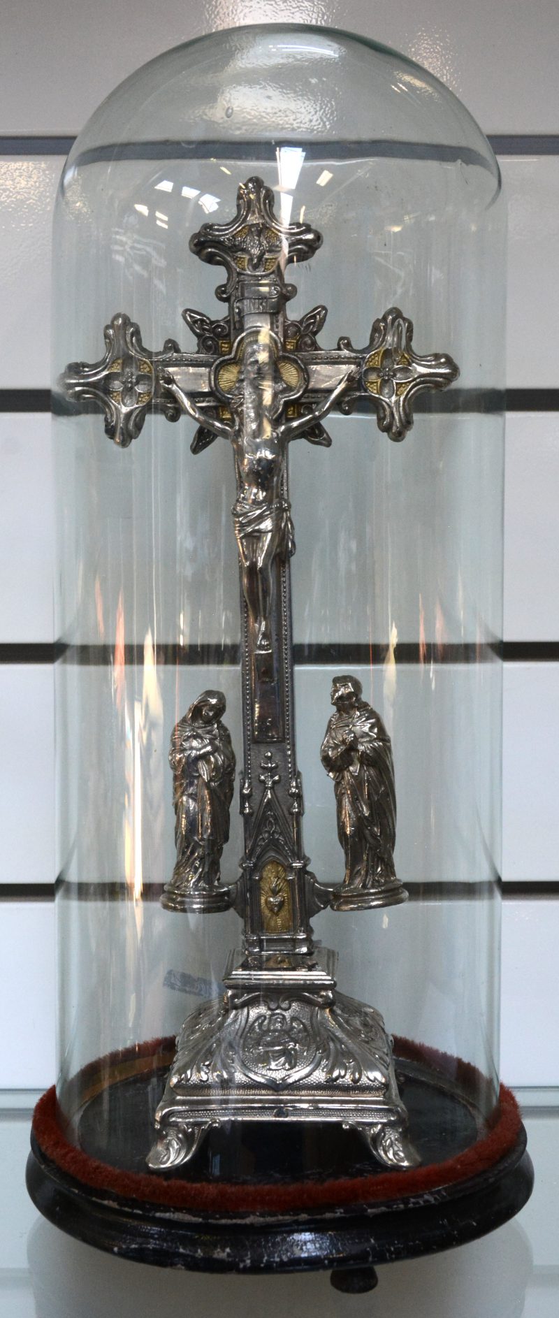 Een verzilverd metalen kruisbeeld onder stolp.