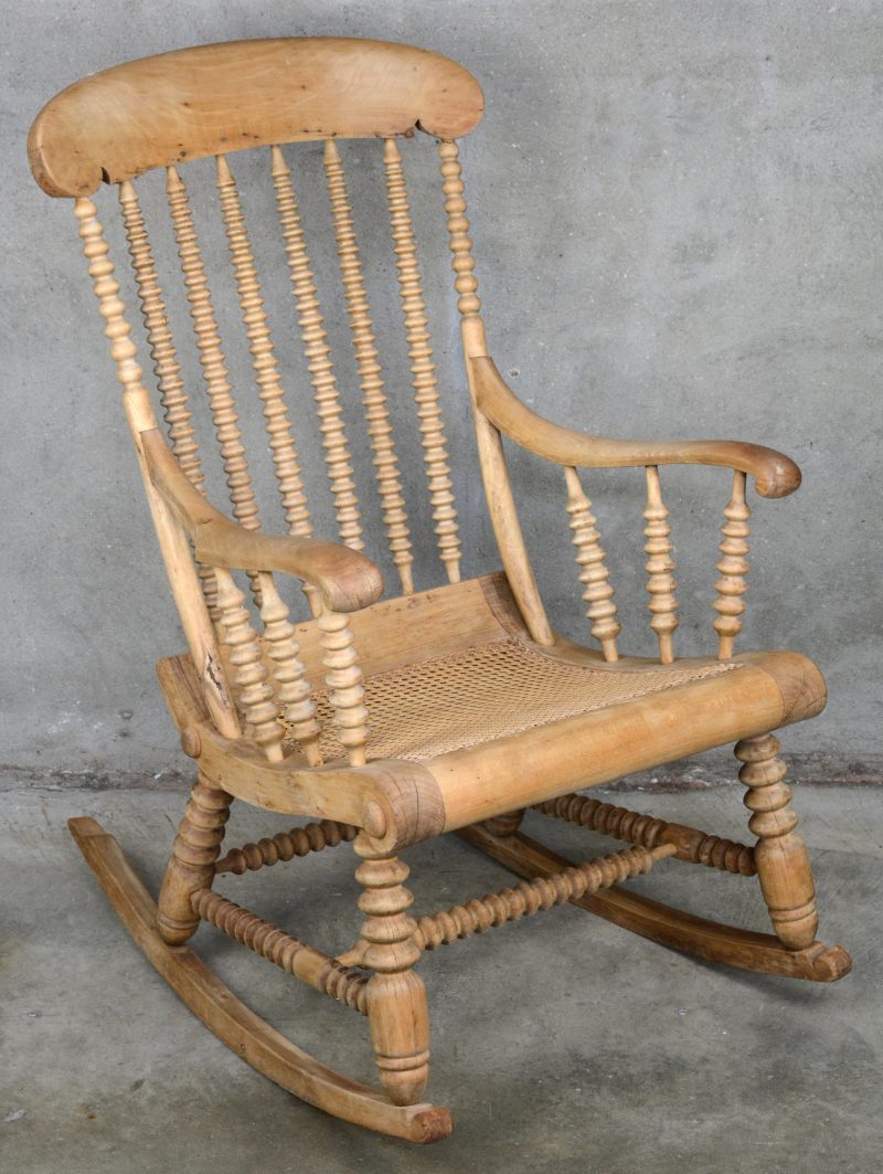 Een Amerikaanse schommelstoel van geloogd notenhout met gecanneerde zit.