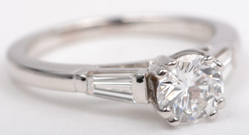 Een 18 K witgouden ring bezet met een centrale briljant van 0,76 ct. E SI1. en twee baguettes met een gezamenlijk gewicht van +- 0,40 ct. Met certificaat.