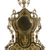 Een driedelig koperen schouwgarnituur in eclectische stijl, bestaande uit een pendule en twee vierarmige kandelaars. Glas voor de wijzeplaat gebarsten.