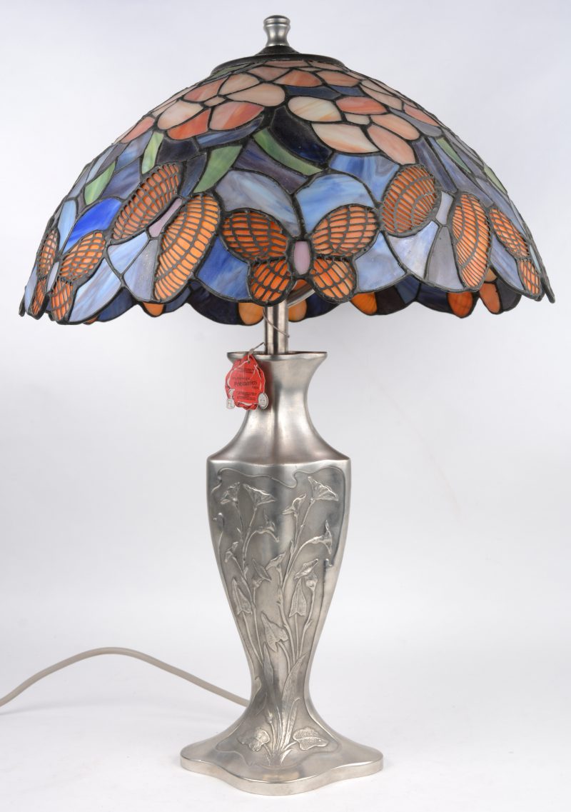 Een schemerlamp met tinnen lampvoet en een kap van glas in lood met vlinders en bloemen.