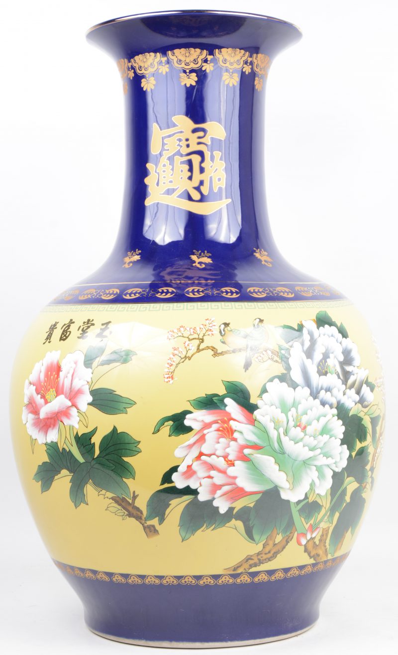 Een grote bolle vaas van Chinees porselein met een decor van pioenen en vogels en met vergulde teksten op kobaltblauwe fond.