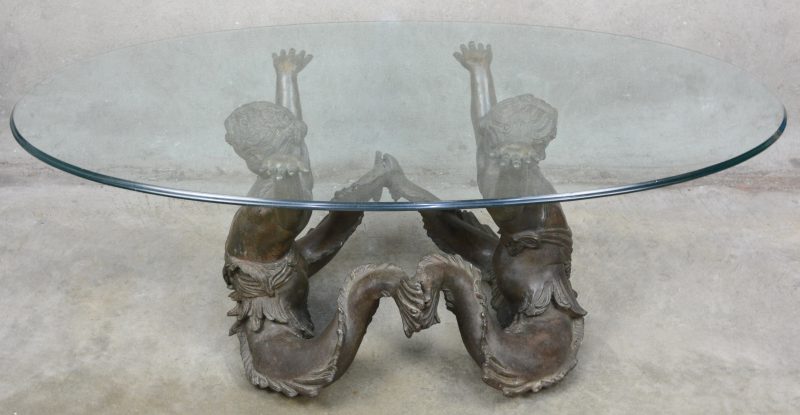 Een salontafel met glazen blad, gedragen door een bronzen voet in de vorm van twee meermannen.