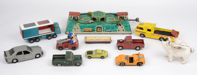 Een lot speelgoed met een geuten spaarvarken een metalen werkende autobaan en autotjes en vrachtwagens.