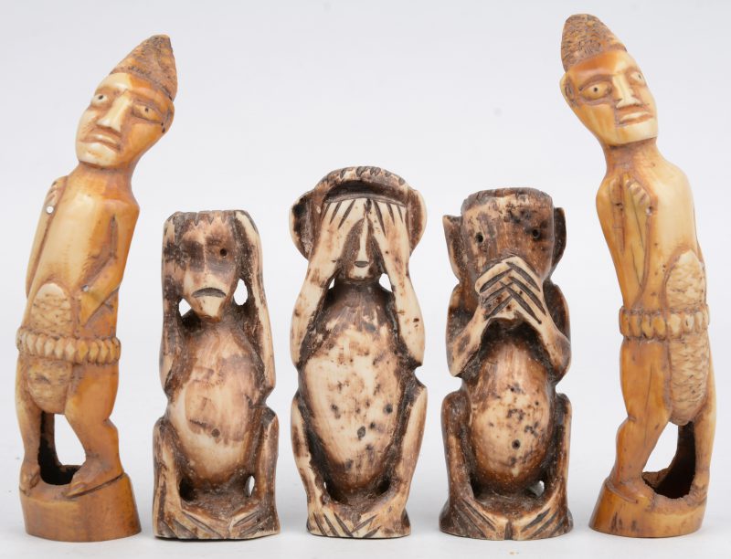 “Horen, zien en zwijgen”. Drie gesculpteerde Afrikaans houten beeldjes. We voegen er twee gesculpteerde wrattenzwijntanden aan toe.