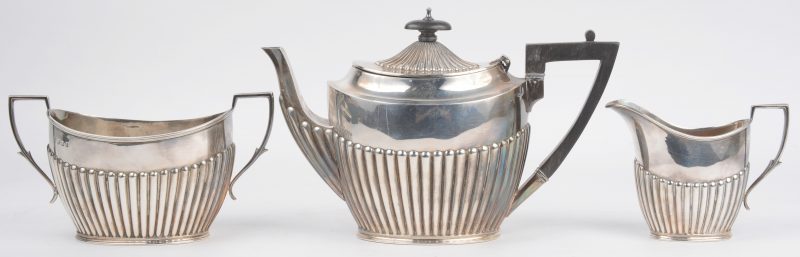 Een driedelige zilveren theeset met geribd decor en de theepot met houten handvat en dekselknop. Schotse keuren.