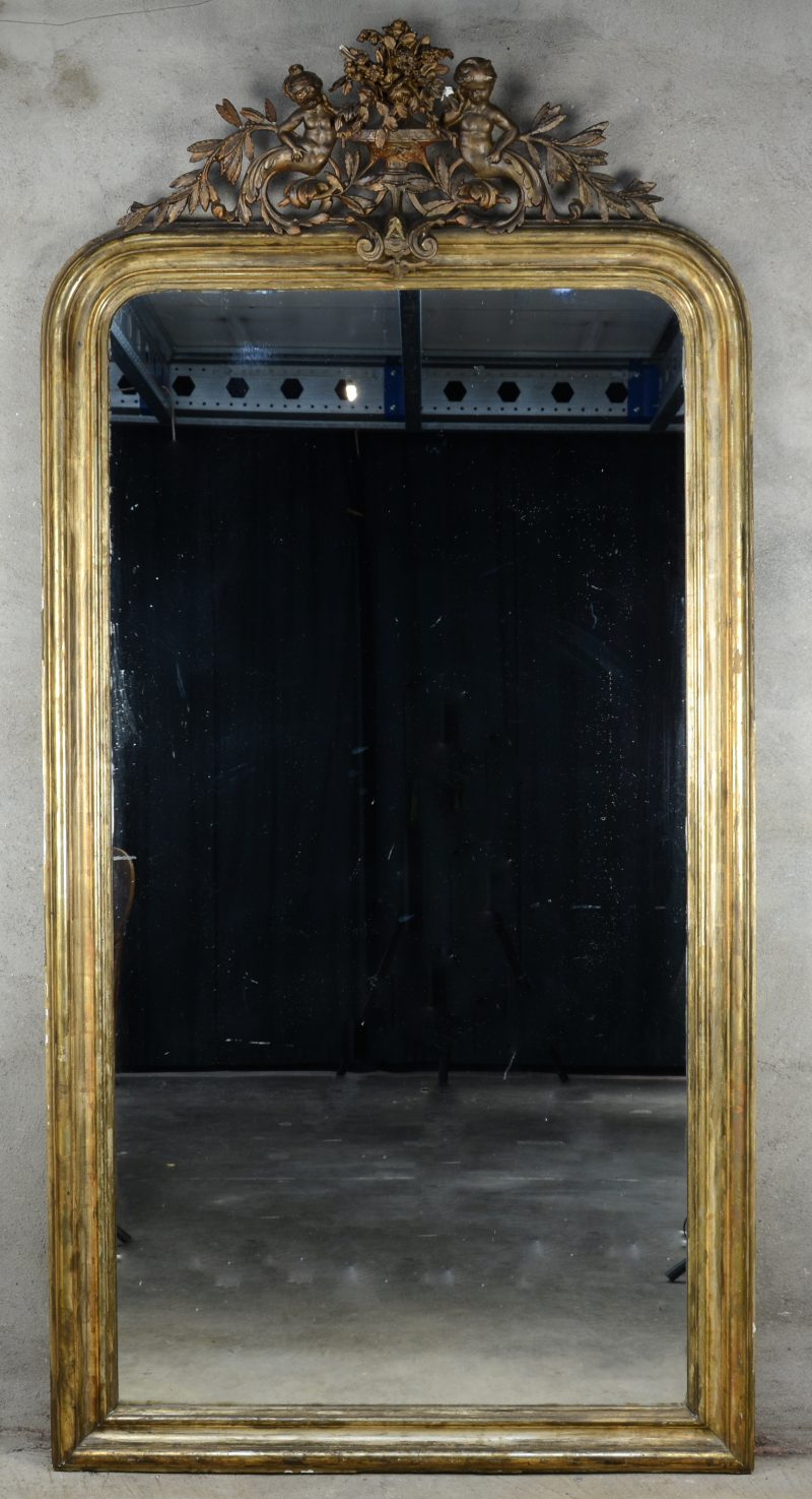 Een grote goudgepatineerde houten schouwspiegel met een kuif in de vorm van een bloementuil, geflankeerd door twee putti.