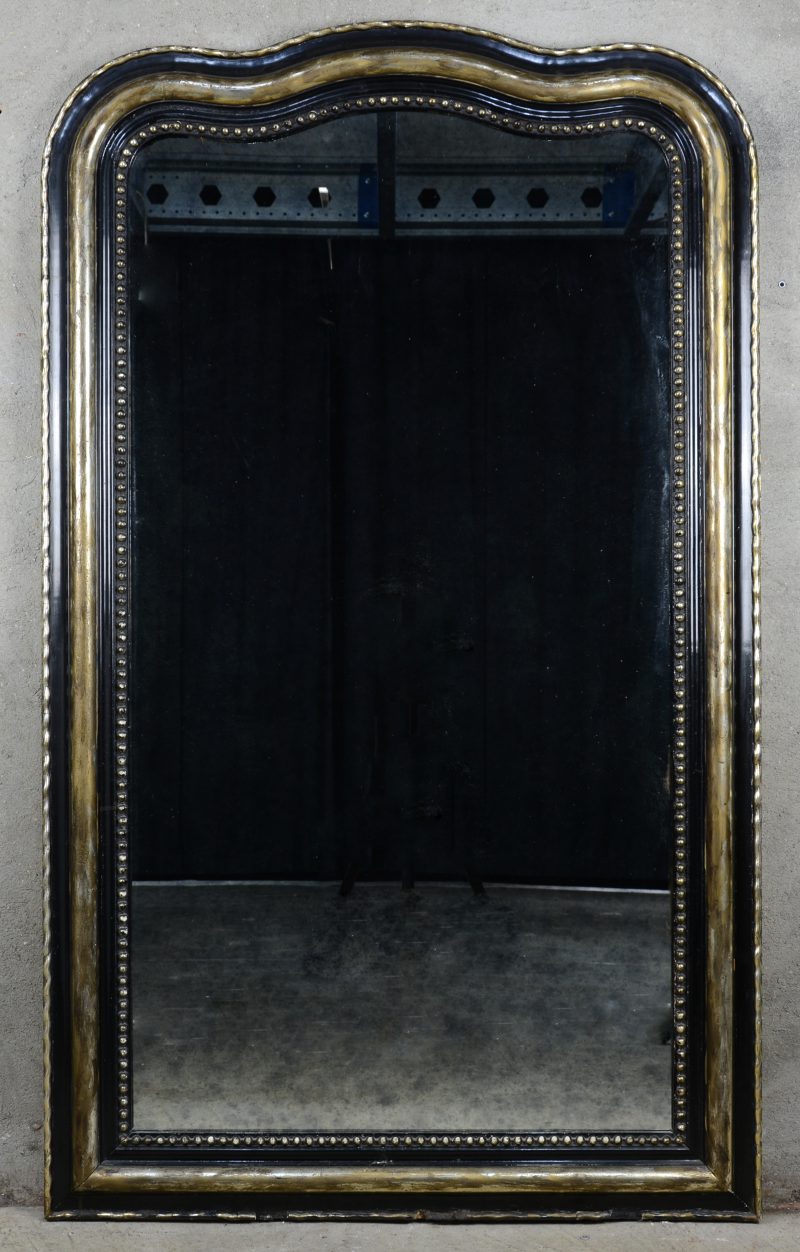 Een schouwspiegel van zwart- en goudgepatineerd hout.