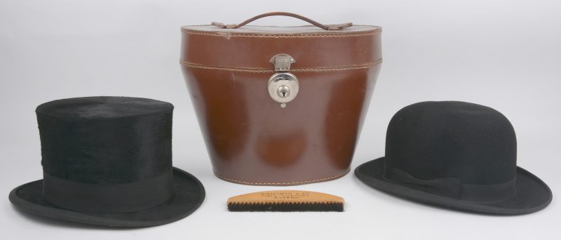 Een hoge hoed, gemerkt van Paul Emy en een bolhoed, gemerkt van Van den Bosch te Leuven. De eerste in houdendoos en met borstel.