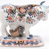Een melkvrouwtje met koe van meerkleurig Delfts aardewerk. Restauratie aan een hoorn en een voetje en een pootje van het krukje manco. Gemerkt van Dextra onderaan.