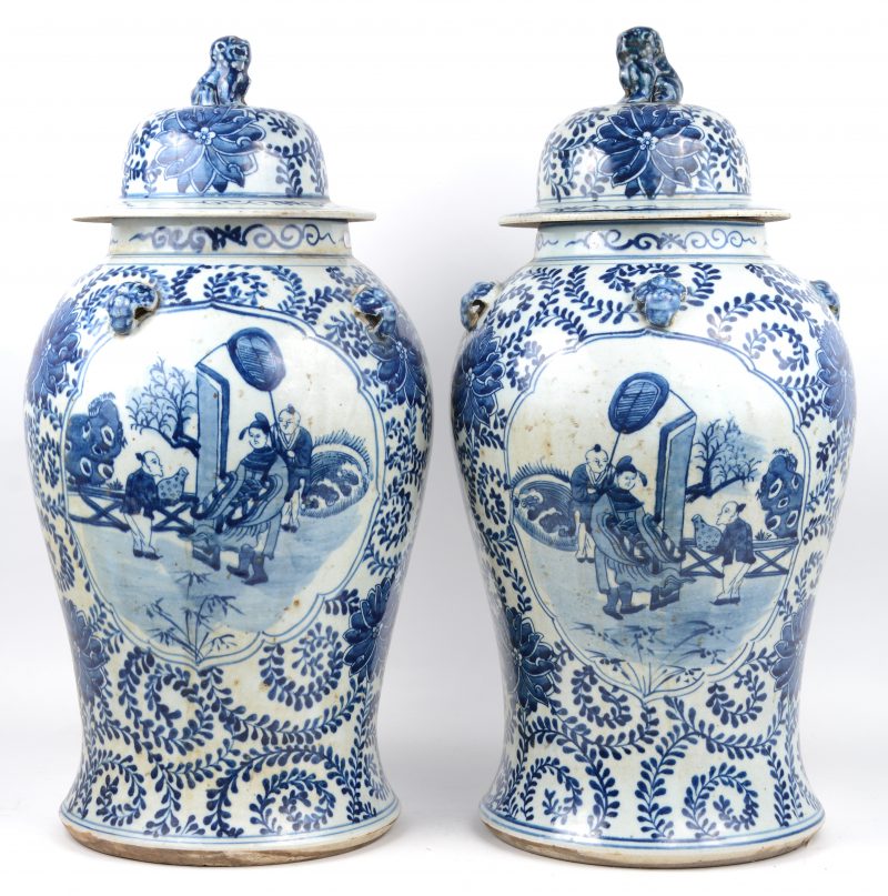 Een paar dekselvazen van Chinees porselein met een blauw op wit decor van personages in cartouches op vegetale achtergrond.