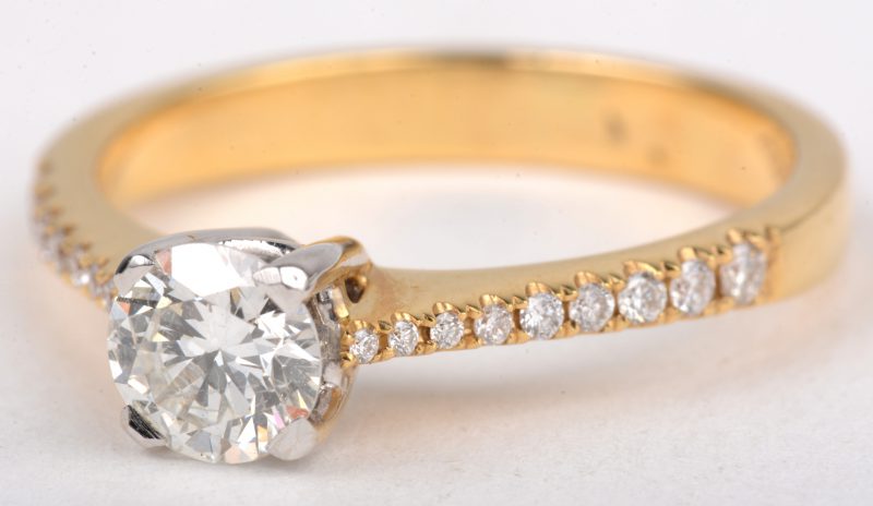 Een 18 K wit en geelgouden ring bezet met een centrale briljant van +- 0,57 ct. FVSI. en briljanten met een gezamenlijk gewicht van +- 0,14 ct.