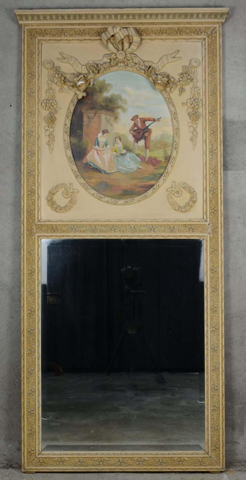 Een spiegel in beigegepatineerde houten lijst in Lodewijk XVI-stijl, versierd met een ovaal olieverfschilderij op paneel met een voorstelling van een muziekspeler bij twee jonge vrouwen.