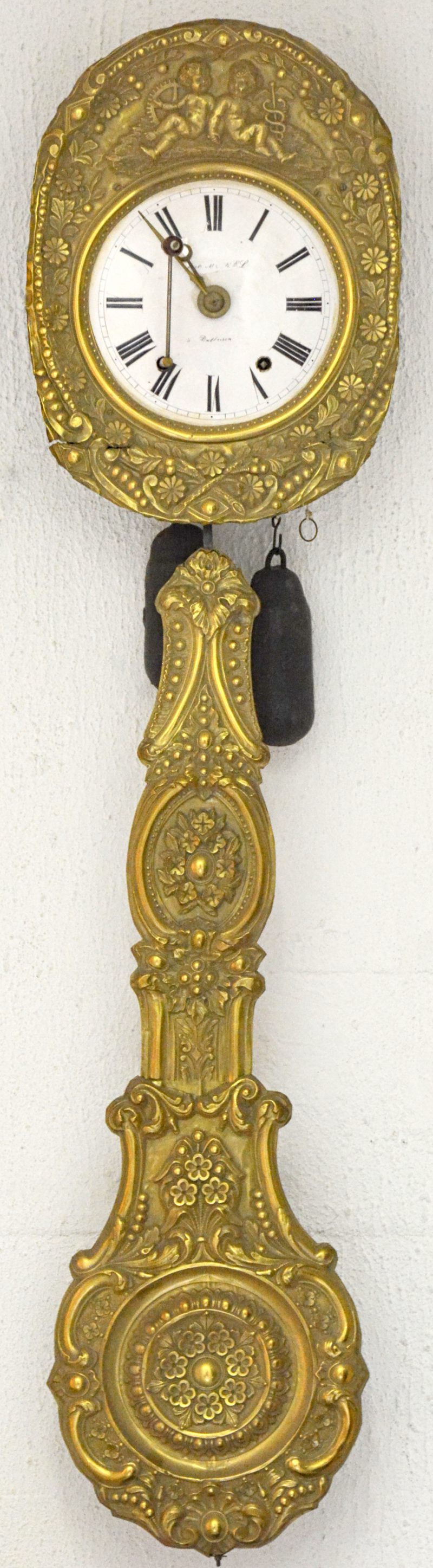 Een comtoiseklok met gedreven messingen slinger en versiering rond de wijzerplaat. Met sleutel en gewichten.