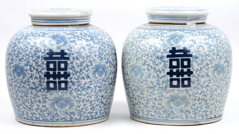 Een paar gemberpotten van Chinees porselein met een blauw op wit decor van tekens op een florale achtergrond.