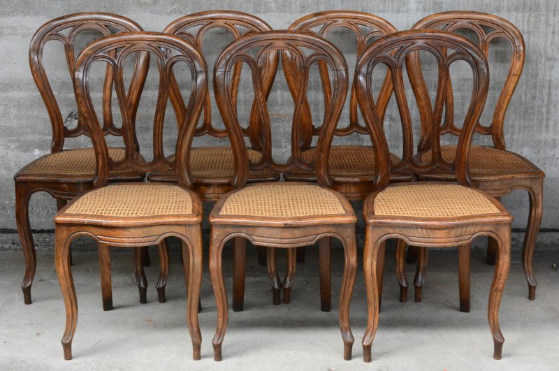 Een reeks van zeven notenhouten stoelen met gecanneerde zit.