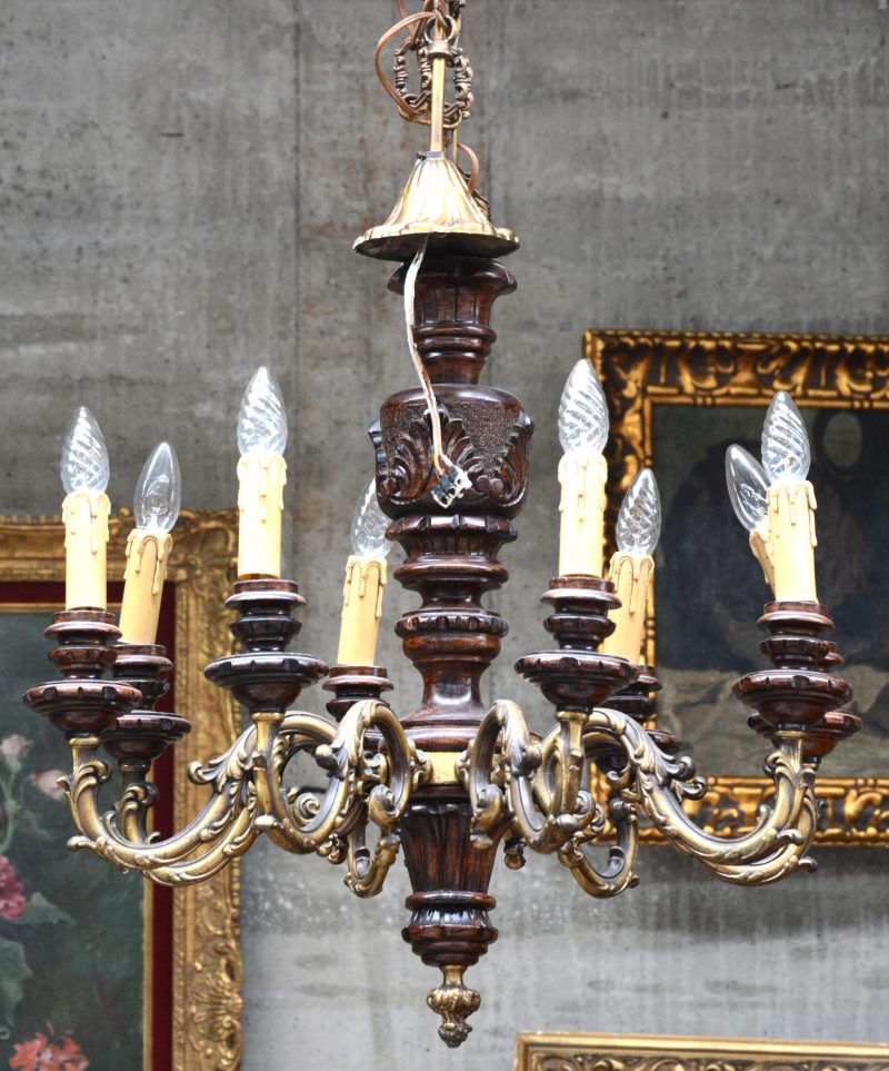 Een achtarmige luchter van verguld messing/ brons en hout, versierd met barokke motieven.