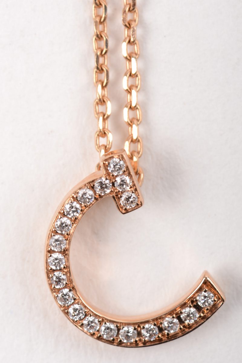 Een 18 K roze gouden ketting met hanger in de vorm van een letter C bezet met briljanten met een gezamenlijk gewicht van +- 0,10 ct.