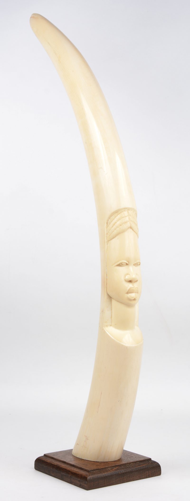 Een Afrikaanse slagtand met gesculpteerd vrouwenhoofd. Op houten voetstuk.