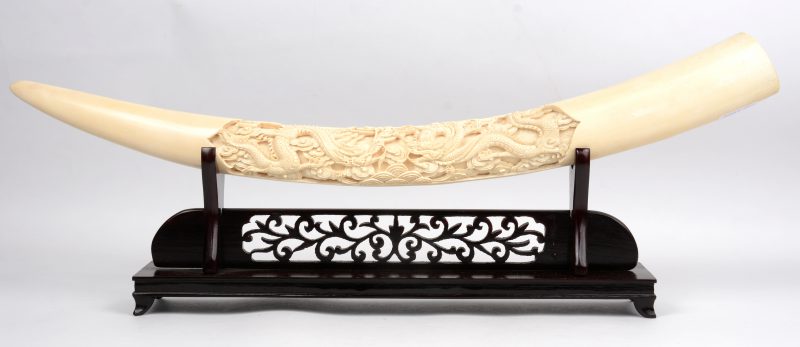 Een Chinees ivoren slagtand met gesculpteerd drakendecor. Op houten staander.