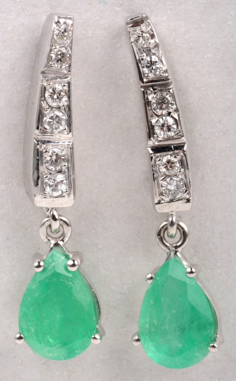 Een paar 18 K witgouden oorbellen bezet met diamanten met een gezamenlijk gewicht van +- 0,20 ct. en twee druppelvormige smaragden met een gezamenlijk gewicht van +- 2 ct.