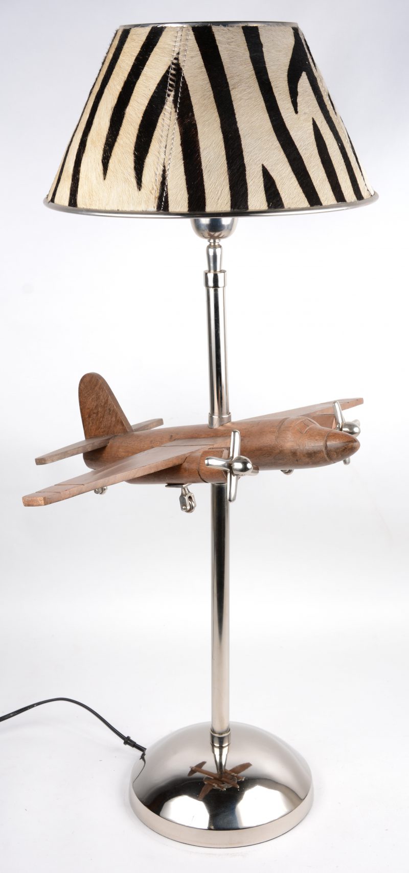 Een moderne chromen lamp met een houten propellervliegtuig en met een kantelbare kap met zebravacht.