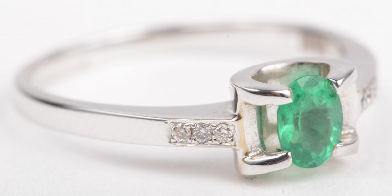 Een 18 K witgouden ring bezet met zes kleine briljantjes en een centrale smaragd van +- 0,35 ct.