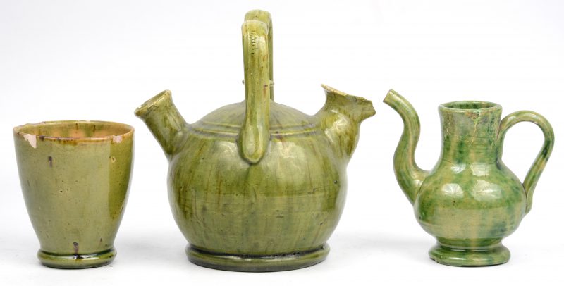 Een keteltje, een theepotje en een beker van groengeglazuurd aardewerk. Beker met schilfer.
