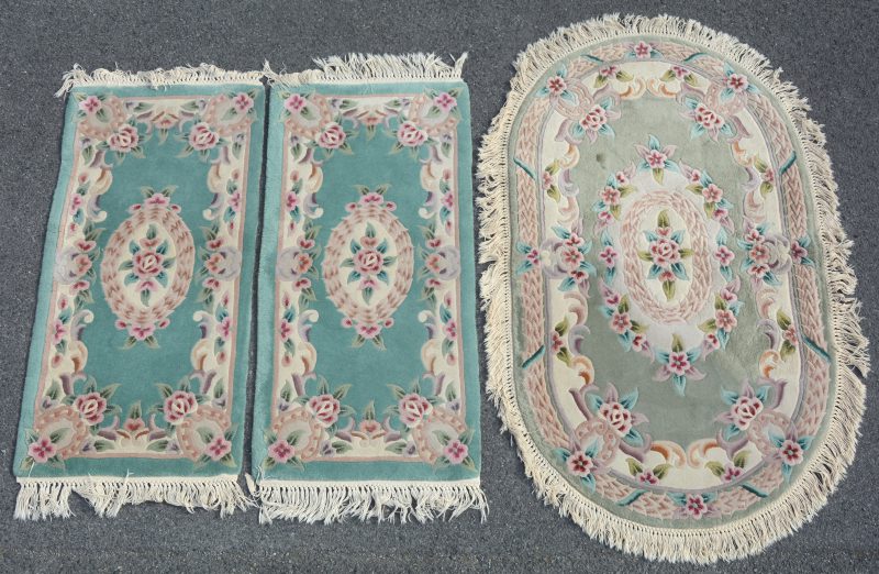 Een lot van een ovaal en twee rechthoekige Chinese wollen karpetjes.