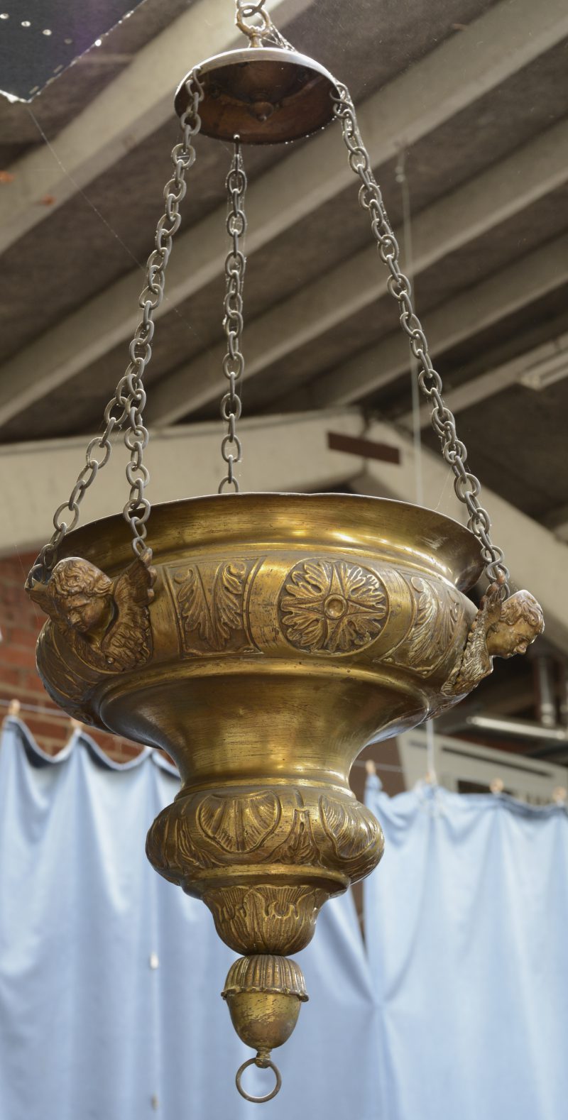 Een barokke godslamp van gedreven geel koper. Versierd met drie gevleugelde engelenkopjes.