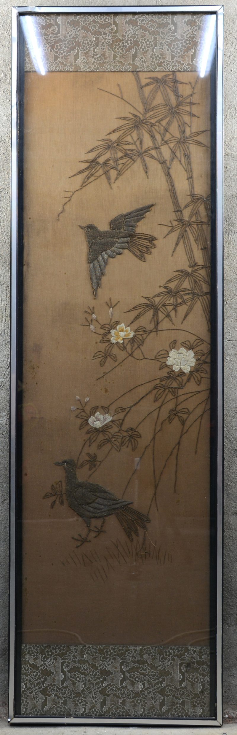 Een groot ingelijst Chinees borduurwerk met een voorstelling van vogels en bloeiende pioenen. Met zilverbrokaat. Begin XXste eeuw.