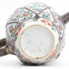 Een theepotje van Chinees porselein met meerkleurig decor van bloemen onder een motief van geweven touw in reliëf. Met zilveren tuit, handvat en deksel. Een haarscheur in het glazuur binnenin aan de bevestiging van het handvat.