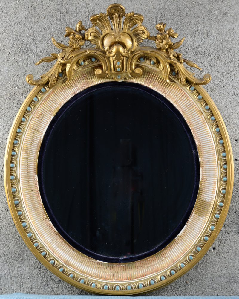 Een ovale spiegel in verguld houten lijst, versierd met een kuif van acantusbladeren en bloemen.