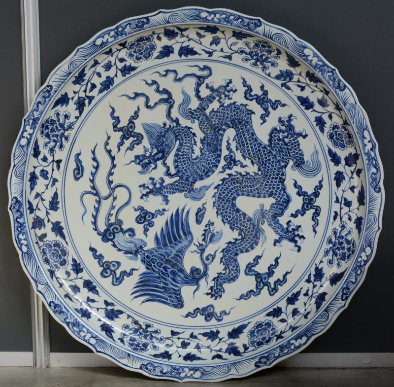 Een grote decoratieve schotel van Chinees porselein met een blauw op wit decor van een draak en een paradijsvogel.