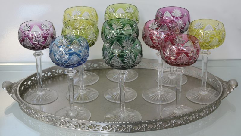 Een reeks van elf geslepen en gekleurde kristallen glazen. Op tinnen dienblad met opengewerkte rand.