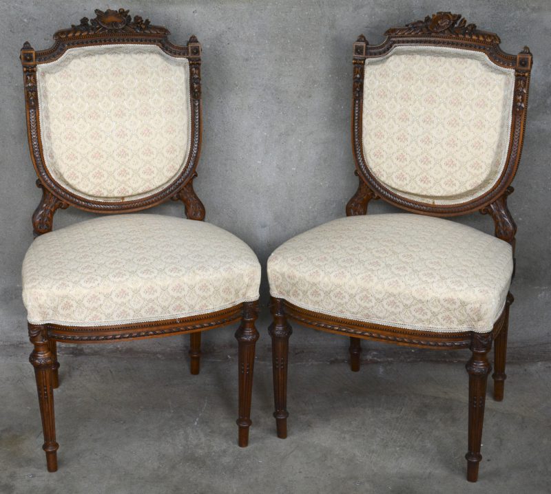 Een paar stoelen in Lodewijk XVI-stijl met fijn gesculpteerde versieringen, waarbij één met een schilderspalet in de rug en de andere met een vrouwenportret.