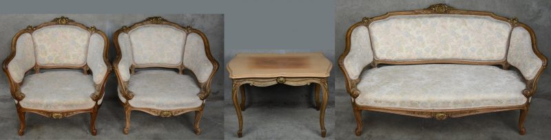 Een driedelig salongarnituur in Lodewijk XV-stijl van gebeeldhouwd notenhout, bestaande uit twee fauteuil en een zitbank. We voegen er een salontafeltje aan toe.