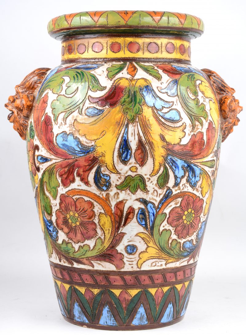 Een majolica vaas met meerkleurig bloemen- en plantendecor en met koppen als handvatten.