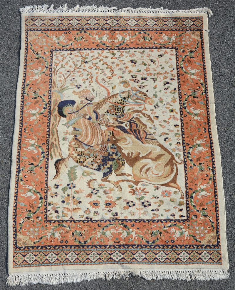Een handgeknoopt Perzisch wollen karpetje met een jachtscène in het decor. Kleine snee in de rechter bovenhoek.