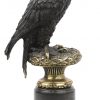 Een adelaar van donker gepatineerd brons op zwart stenen sokkel.