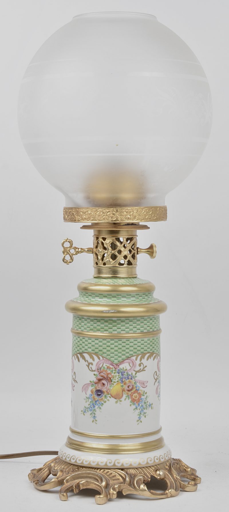 Porceleinen lampvoet met glazen bolle kap. Versiert met bloemen en groen patroon. Met messingen details. Gemerkt.