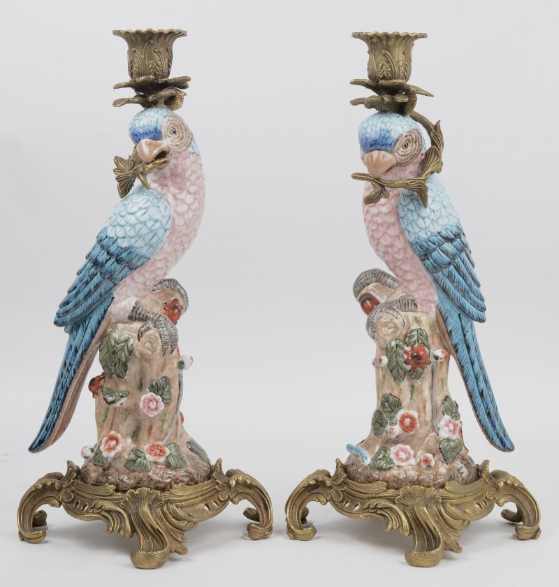 Een paar kandelaars van verguld brons, gedragen door meerkleurig porseleinen papegaaien.