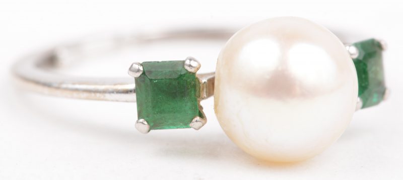Een 18 K witgouden ring bezet met twee smaragden met een gezamenlijk gewicht van +- 0,30 ct. en een parel.