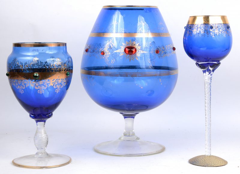 Een drie verschillende bolle glazen met kleurloze voet en blauwe kelk, versierd met vergulde motieven en glazen kralen.