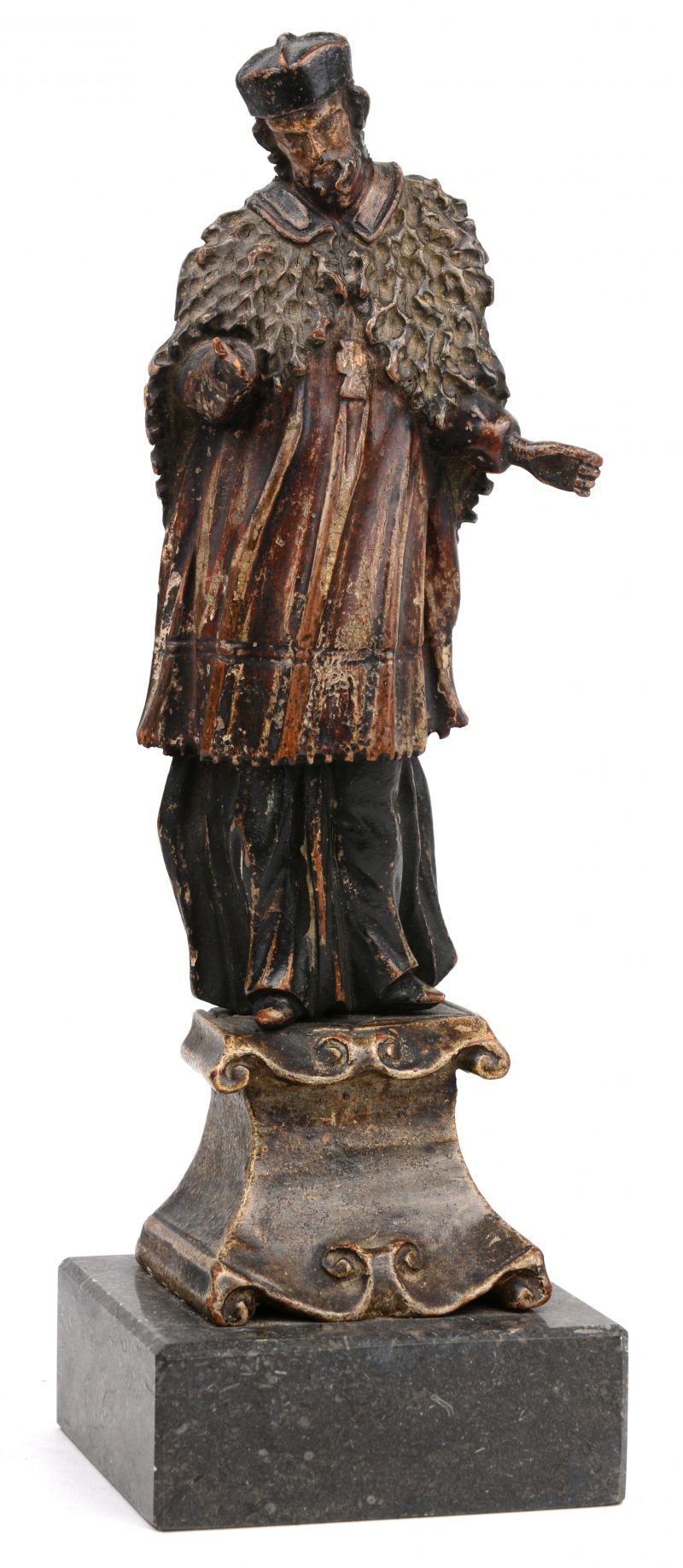 “Bisschop”. Een fijn gesneden en gepolychromeerd houten beeldje. Tijdperk barok. Staf en vingers manco. Later op granieten voetstuk bevestigd.
