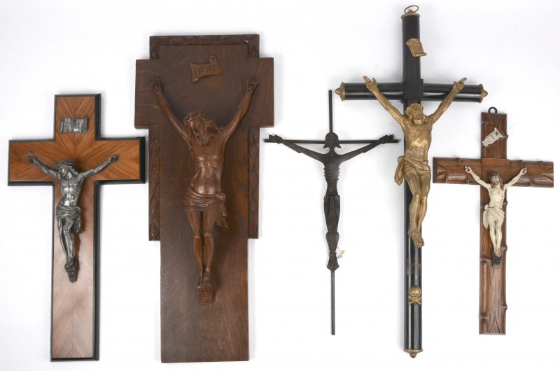 Een lot van vijf verschillende kruisbeelden, waarbij één van zamak, één van tin, één van gepolychromeerd metaal/ kunststof, één smeedijzeren en één gebeeldhouwd houten.