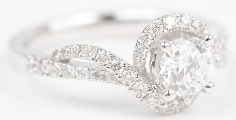 Een 18 K witgouden ring bezet met een centrale diamant van +- 0,70 ct. FVVS1 en briljanten met een gezamenlijk gewicht van +- 0,48 ct.