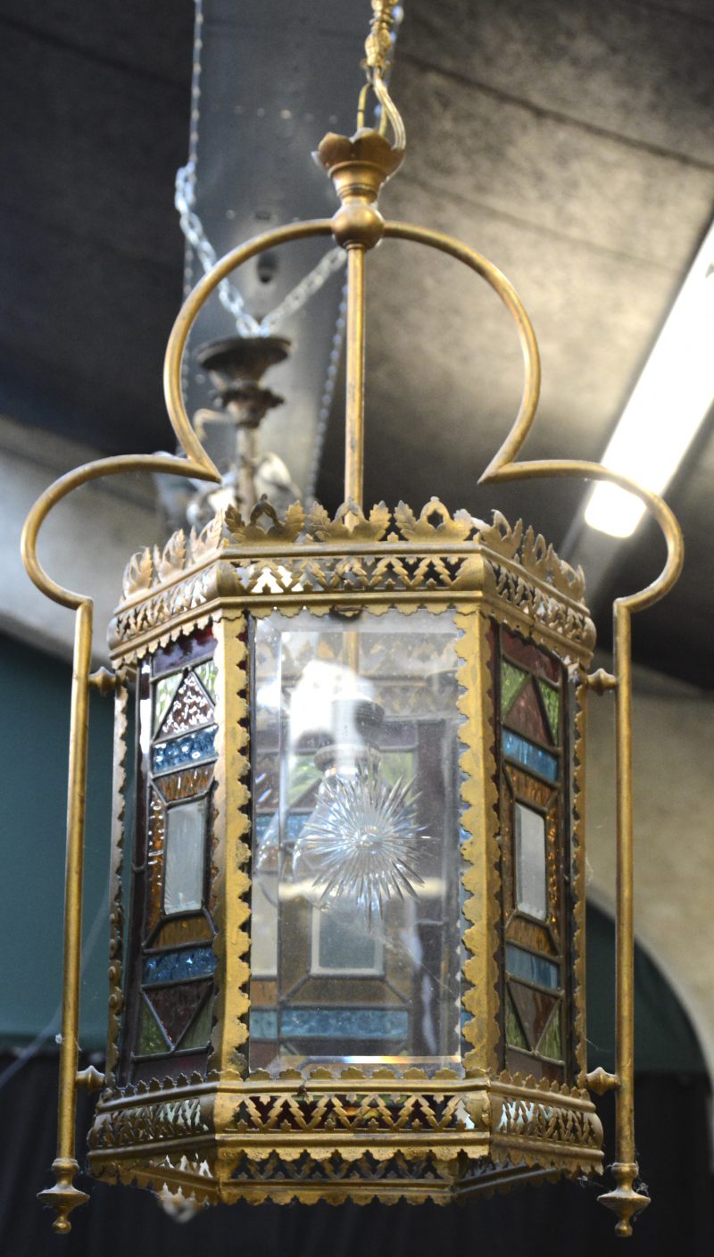 Een zeshoekige lantaarn van messingmet drie kleurloze glaasjes en drie met glas in lood.