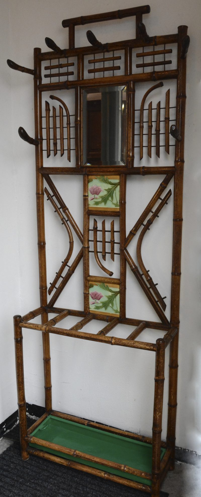 Een bamboehouten staande halkapstok met een spiegeltje en twee aardewerken tegels met bloemendecor.