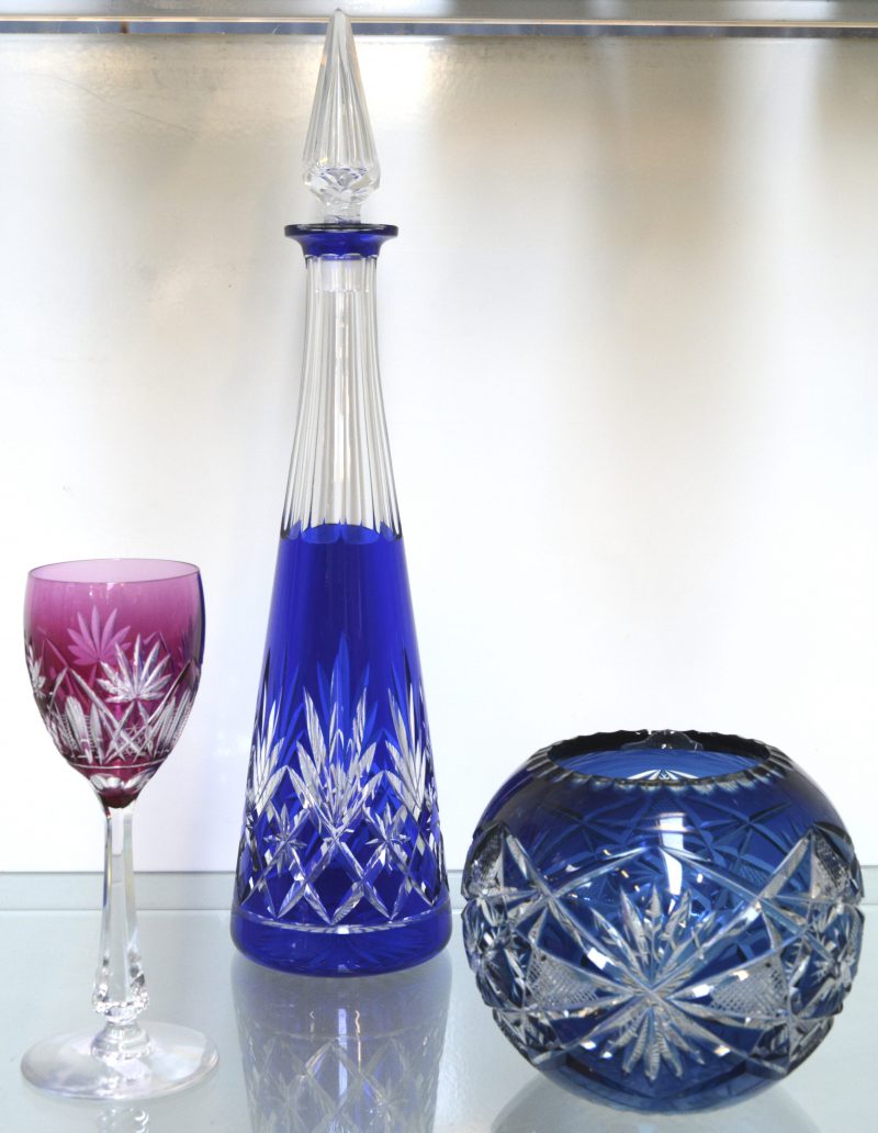Een lot van drie stuks geslepen en gekleurd Boheems kristal (barstje aan binnenrand), bestaande ut een bol vaasje, een karaf en een wijnglas.